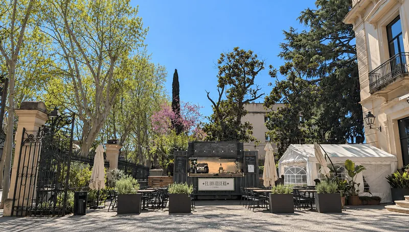 Terraza de El (Bon) Tiberi, en Sant Cugat, con mesas bajo los árboles y un quiosco con pizarra al fondo